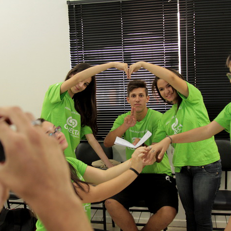 Grupo de pessoas com camisetas verdes do projeto Conecta, onde duas mulheres estão formando um coração com as mãos e tem um homem ao centro.