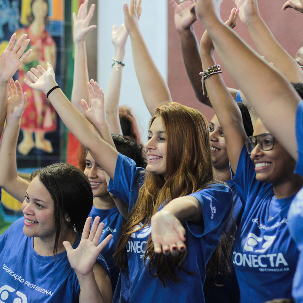 Um grupo de pessoas vestindo a camiseta azul do projeto Conecta, sorrindo e com as mãos levantadas em sinal de comemoração.