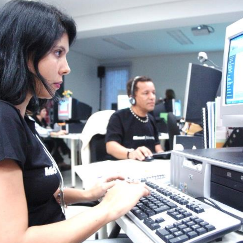 Mulher com camisa preta usando um computador, concentrada em suas tarefas durante o Programa Aluno Monitor.