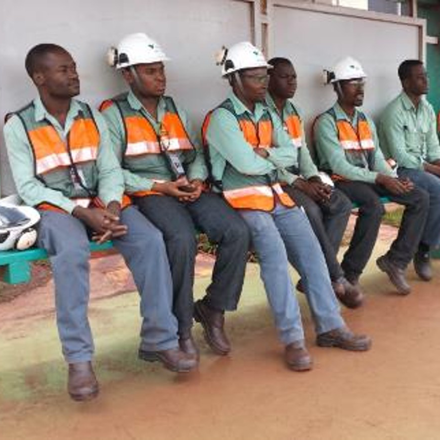 Grupo de homens com capacetes de segurança sentados em um banco durante atividade do Projeto Ferrovia Nacala