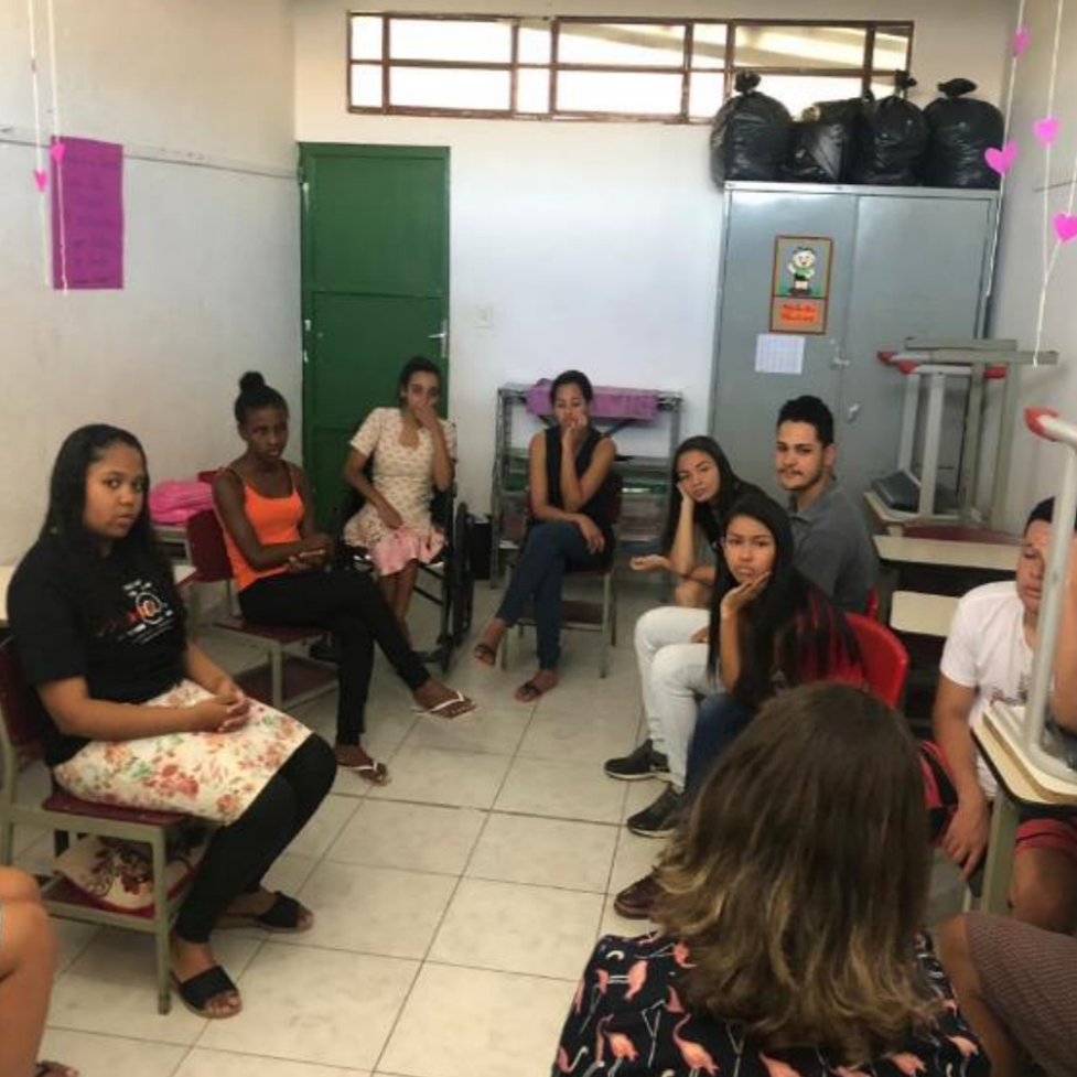 Várias pessoas reunidas sentadas em semicírculo em uma sala de aula, participando de uma atividade colaborativa do projeto Jovem 3.0.